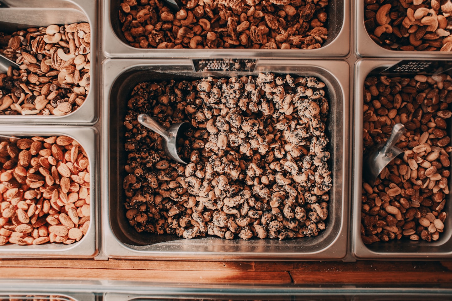 Metalen bakken gevuld met diverse noten in een supermarkt.